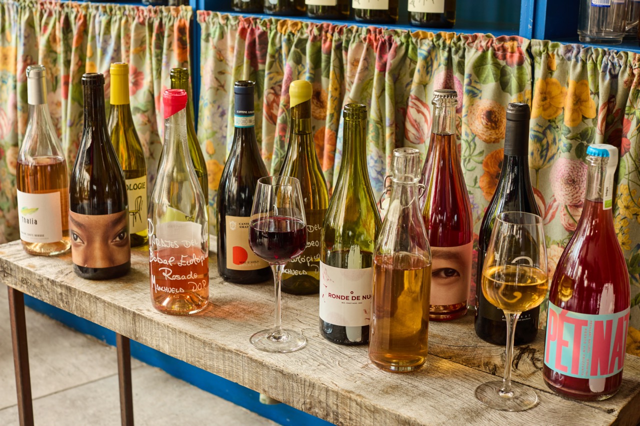 Bottles and glasses of wine on wooden table against flowery curtain