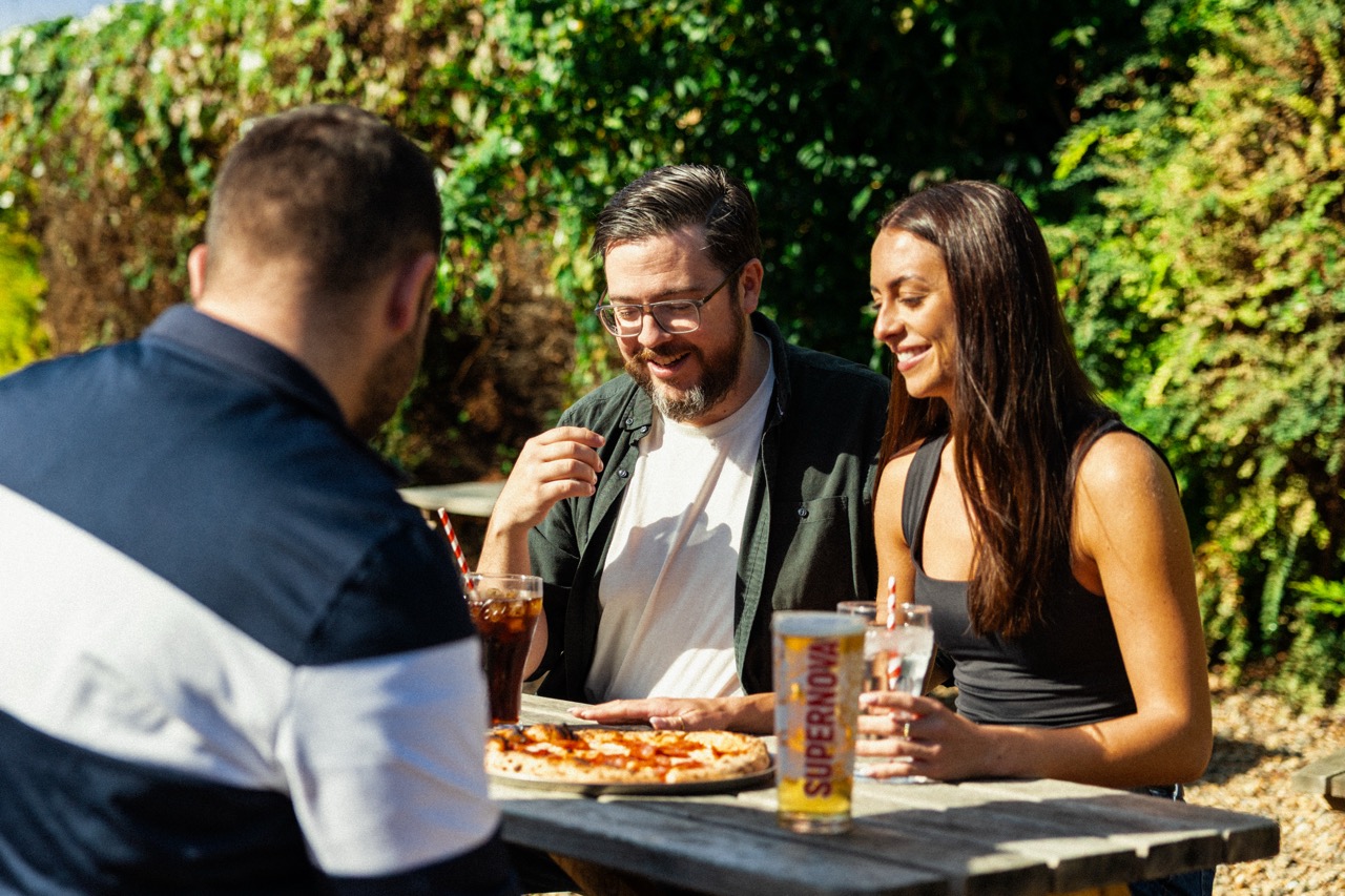 A group of people enjoying a drink together in a sunny Wells & Co. beer garden