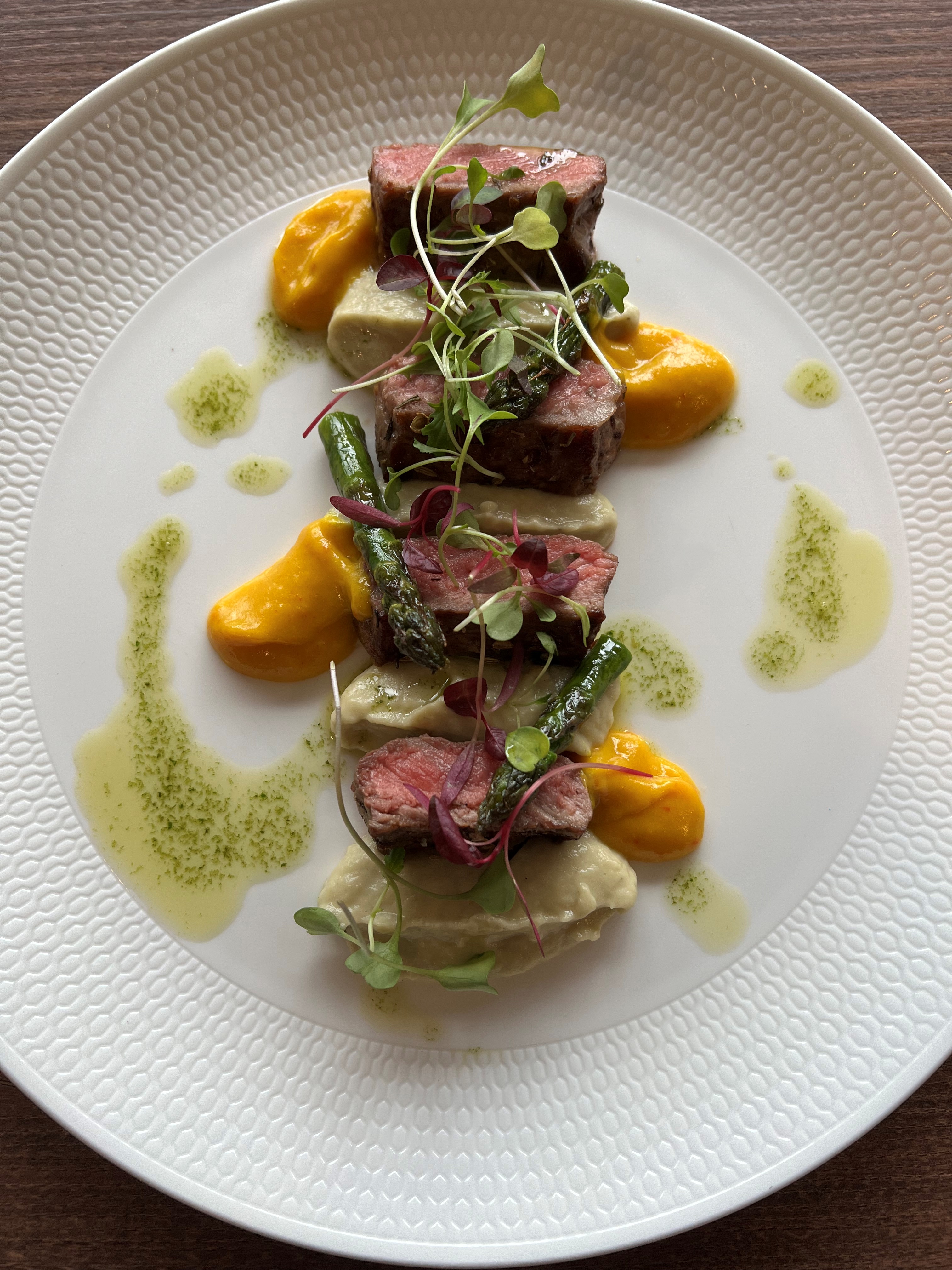Overhead shot of rare sliced lamb with asparagus and a yellow sauce