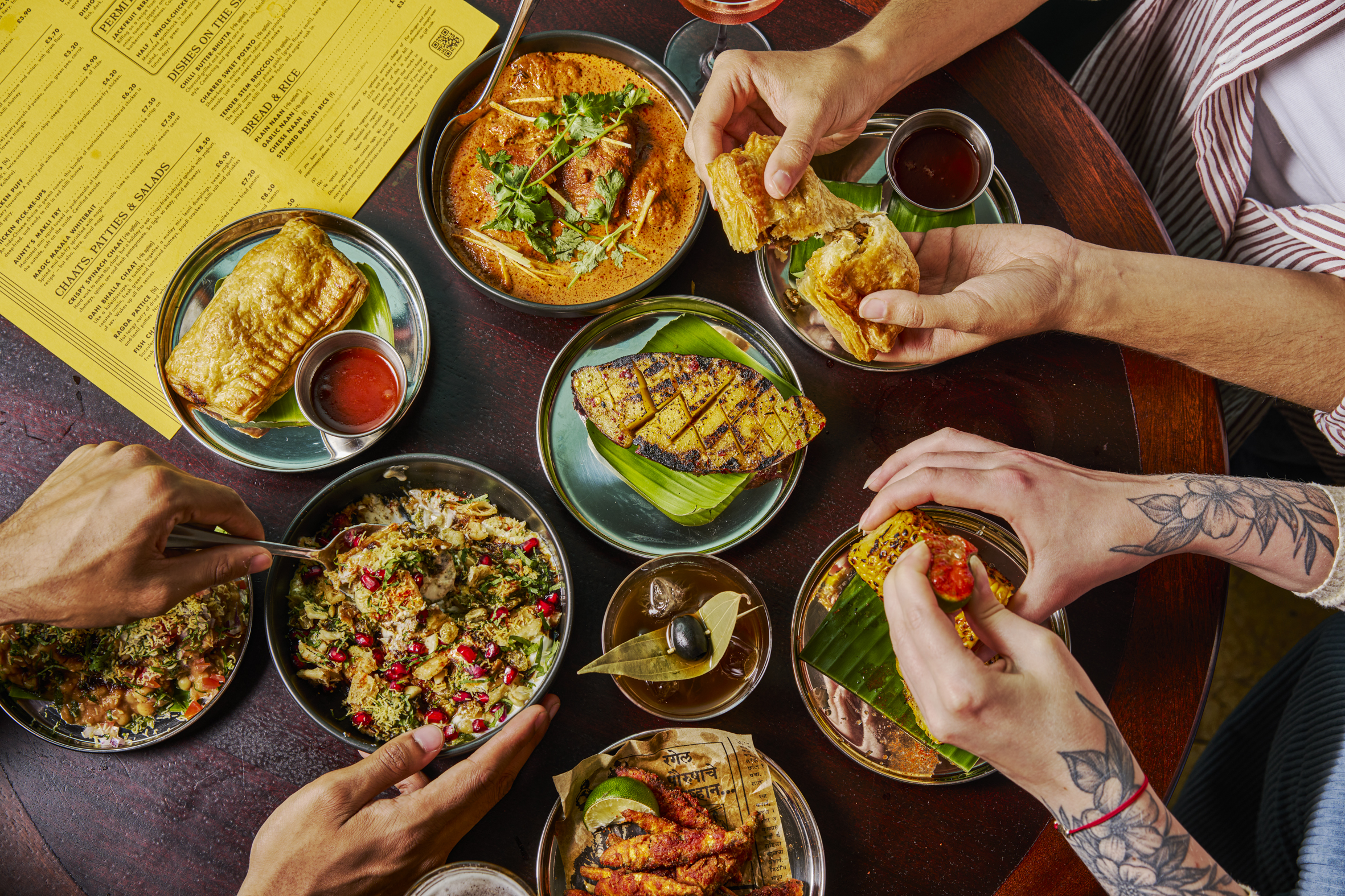 Overhead shot of colourful food in bowls, with hands reaching for it
