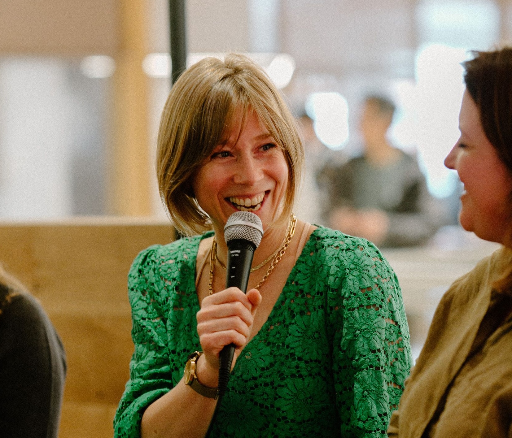 Ceri Gott in a green dress holding a microphone and speaking with Juliane Caillouette Noble
