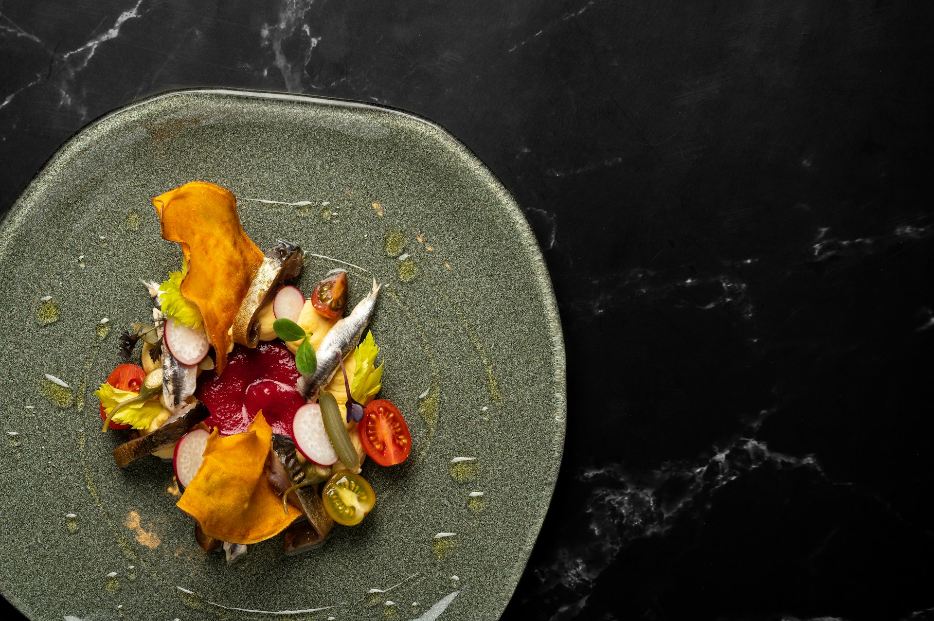 Overhead shot of beautiful vegetable and anchovy dish on dark plate against black marble background