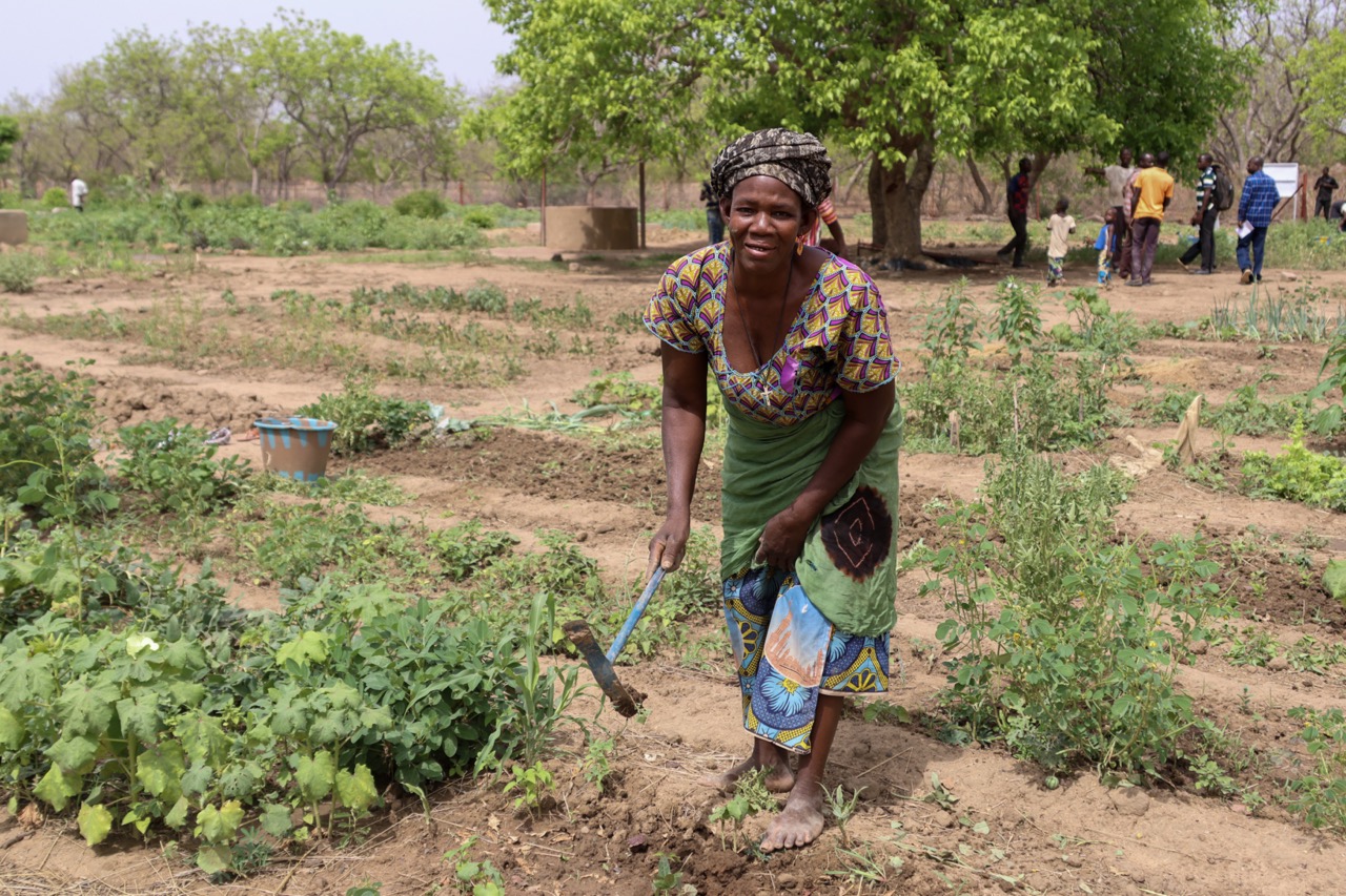 A woman farming in her community garden in Mali, looking up at the camera
