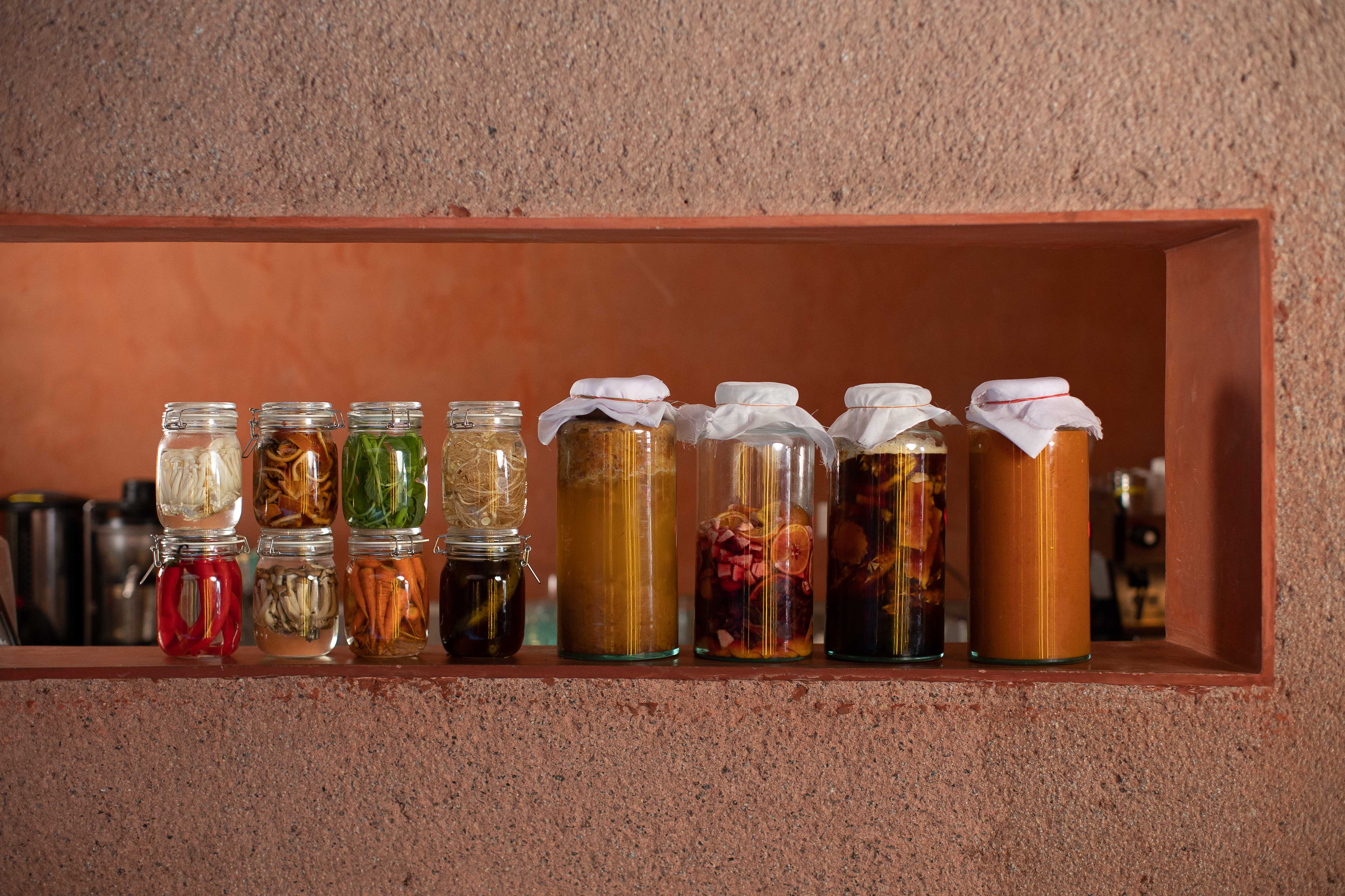 Differently-sized glass jars on a shelf, containing colourful ferments