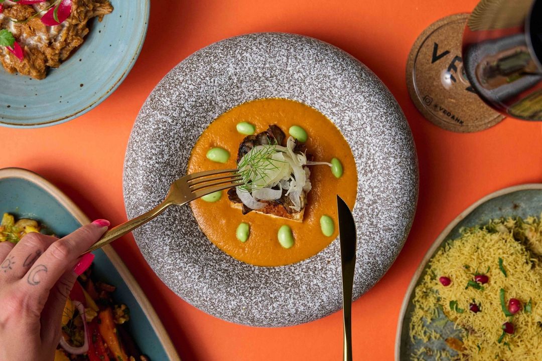 Overhead shot of beautiful saucy food on grey plate, with hands holding knife and fork