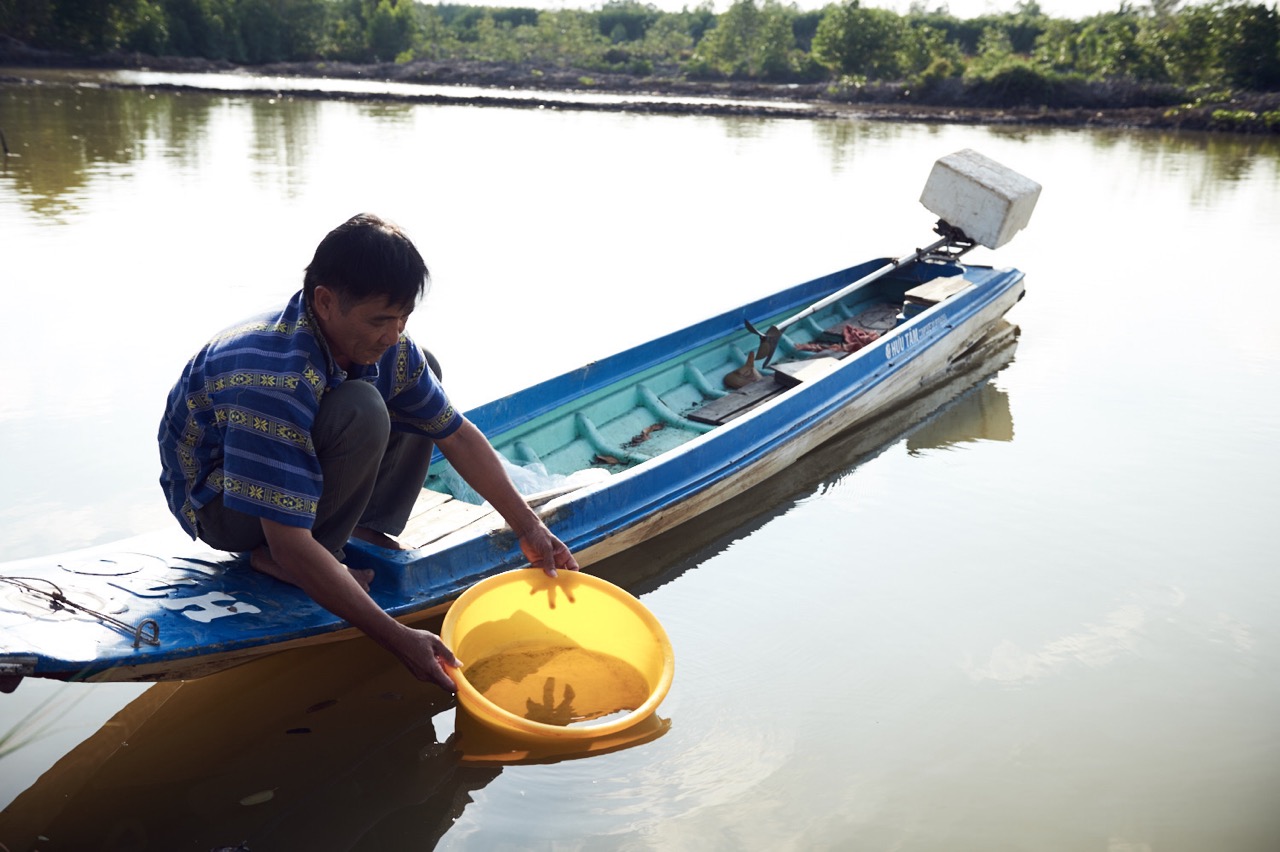 A man crouching in a small row-boat with a yellow bucket