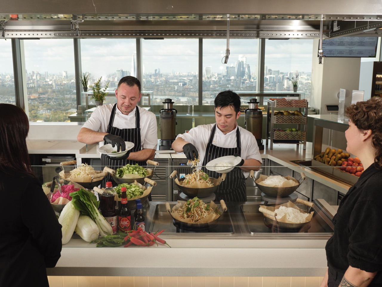 Two members of staff at Restaurant Associates serving food to customers over counter