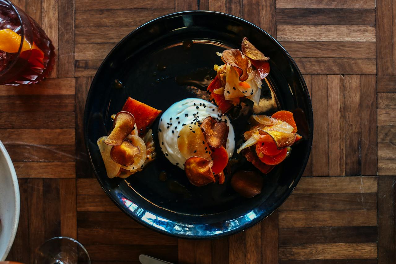 Overhead shot of root vegetable crisps with whipped ricotta on dark plate