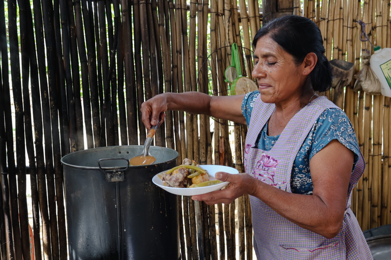 A woman in Mexico ladling a stew out of a big pot into a white bowl