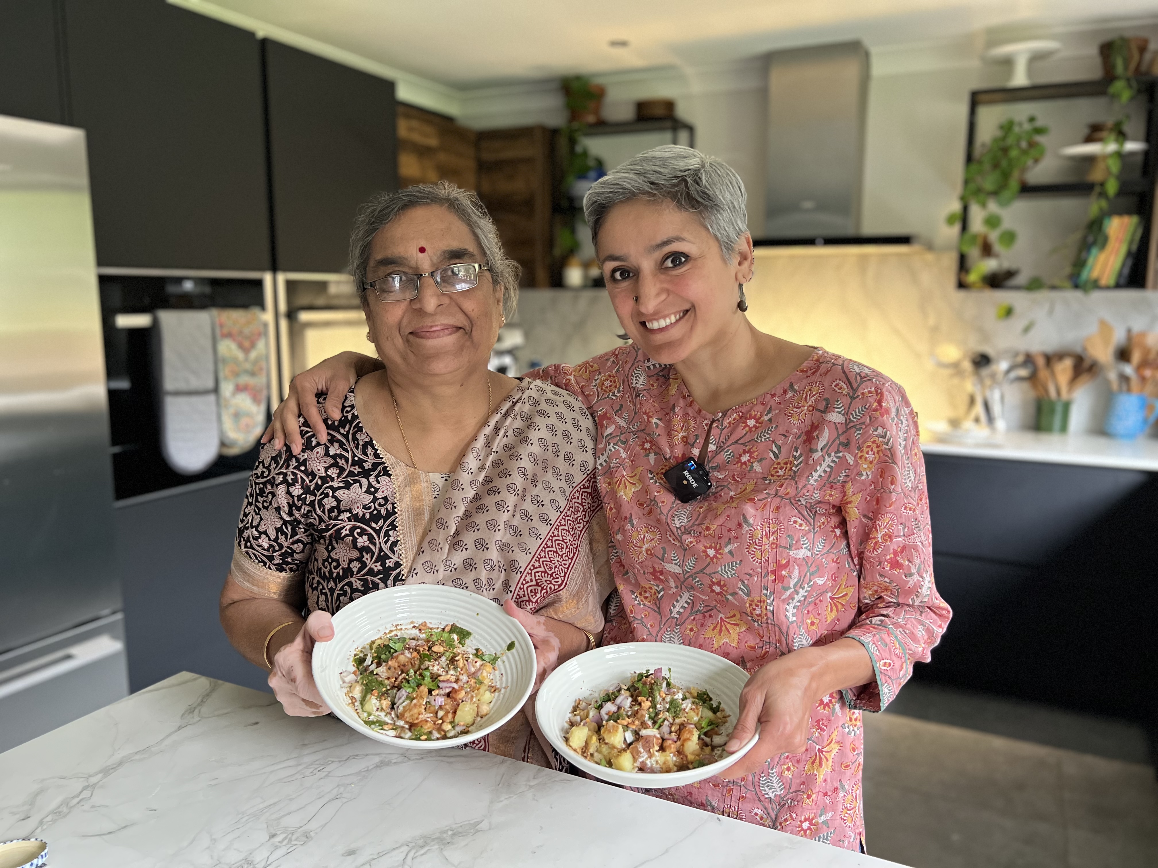 Chetna Makan in the home kitchen with a relative, holding plates of food