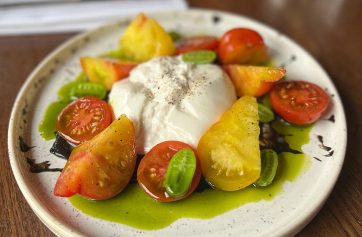 Colourful tomato salad with a ball of burrata in the centre and a green dressing