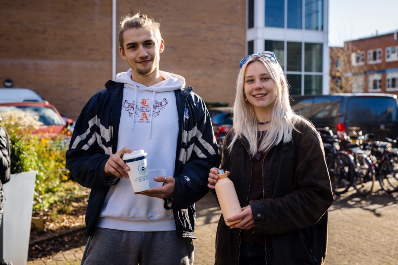 Two students standing outside at Cardiff Metropolitan University holding reusable cups and bottles