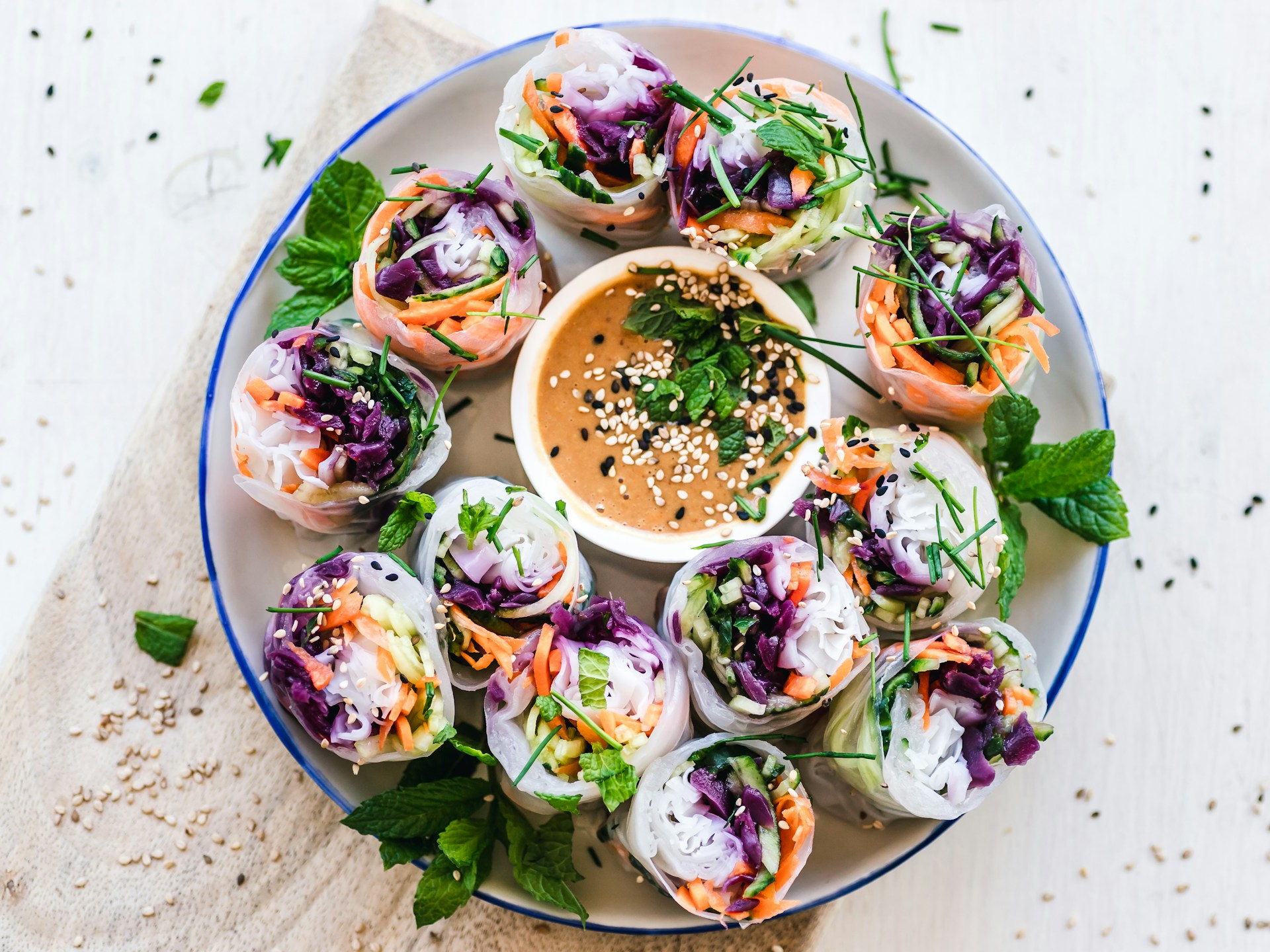 Overhead shot of colourful rice paper rolls filled with vegetables, arranged around a bowl of peanut sauce