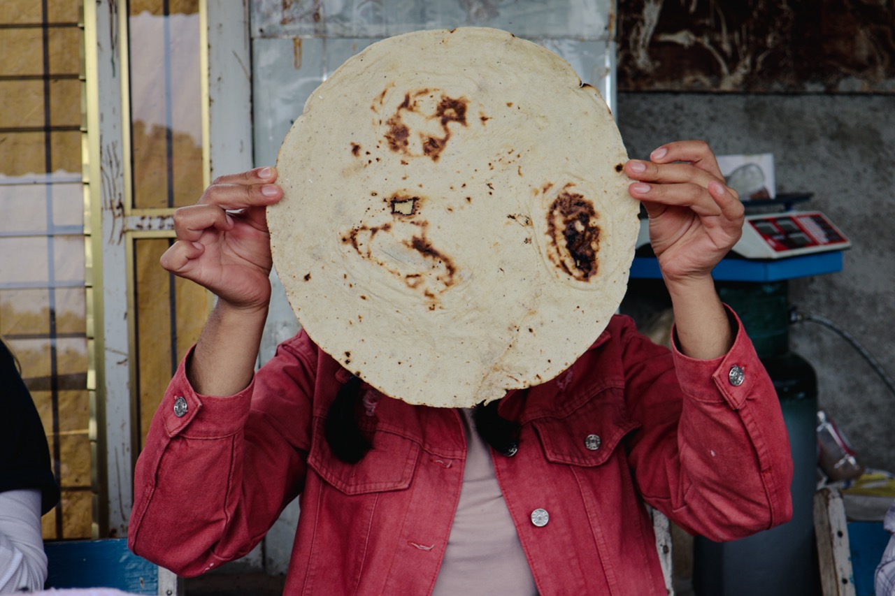 A woman in Mexico holding a homemade tortilla in front of her face