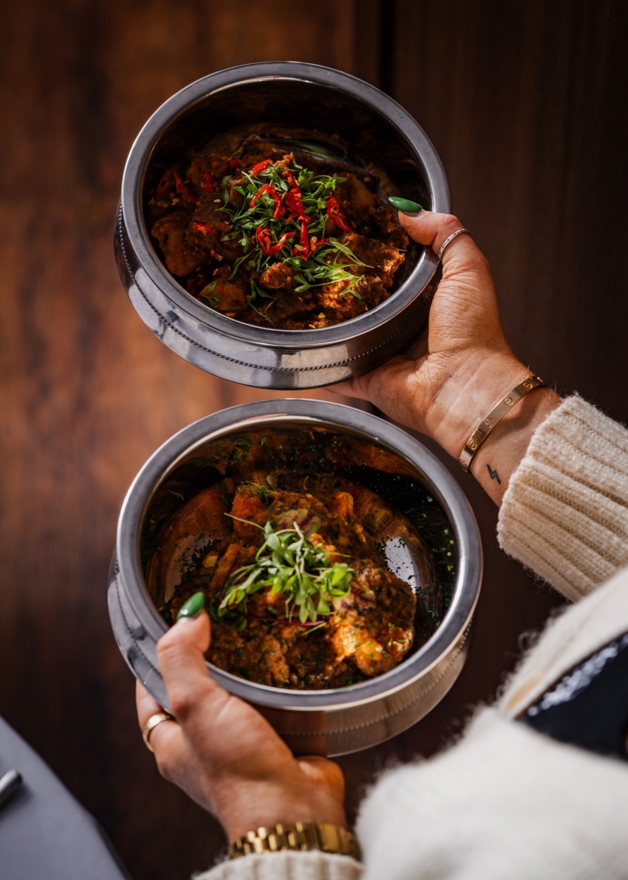 Hands holding two bowls of curry at Lavang