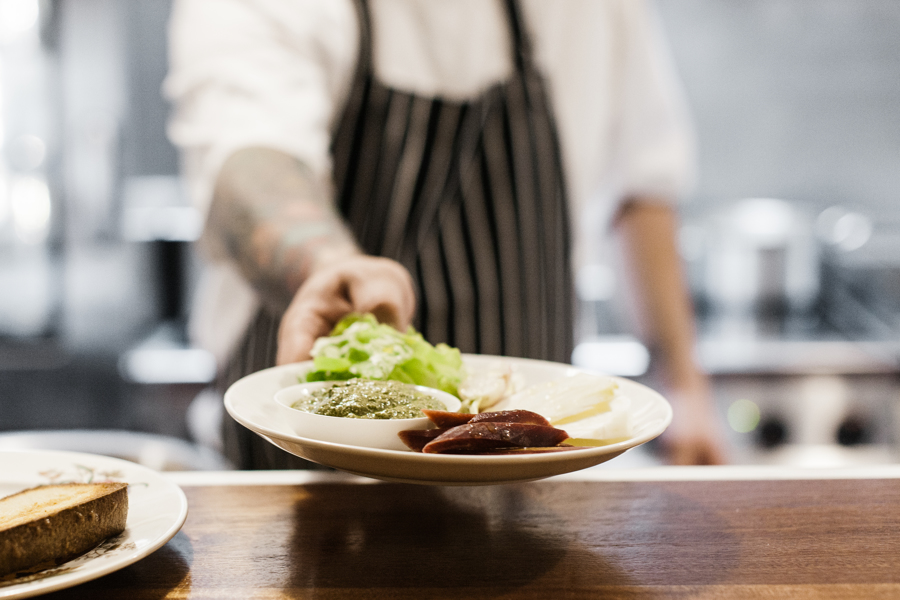 Chef in striped apron holding a plate of food out towards the camera