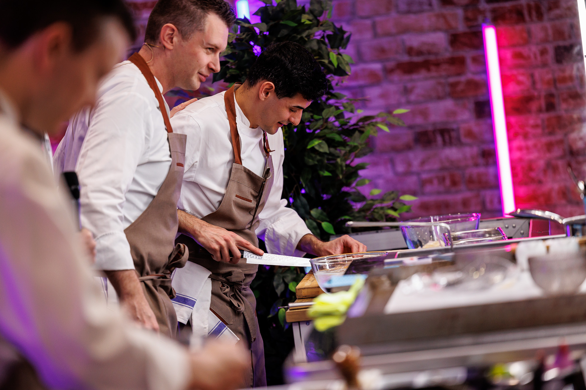 Three male chefs in tan aprons cooking at London's Hotel, Restaurant & Catering show
