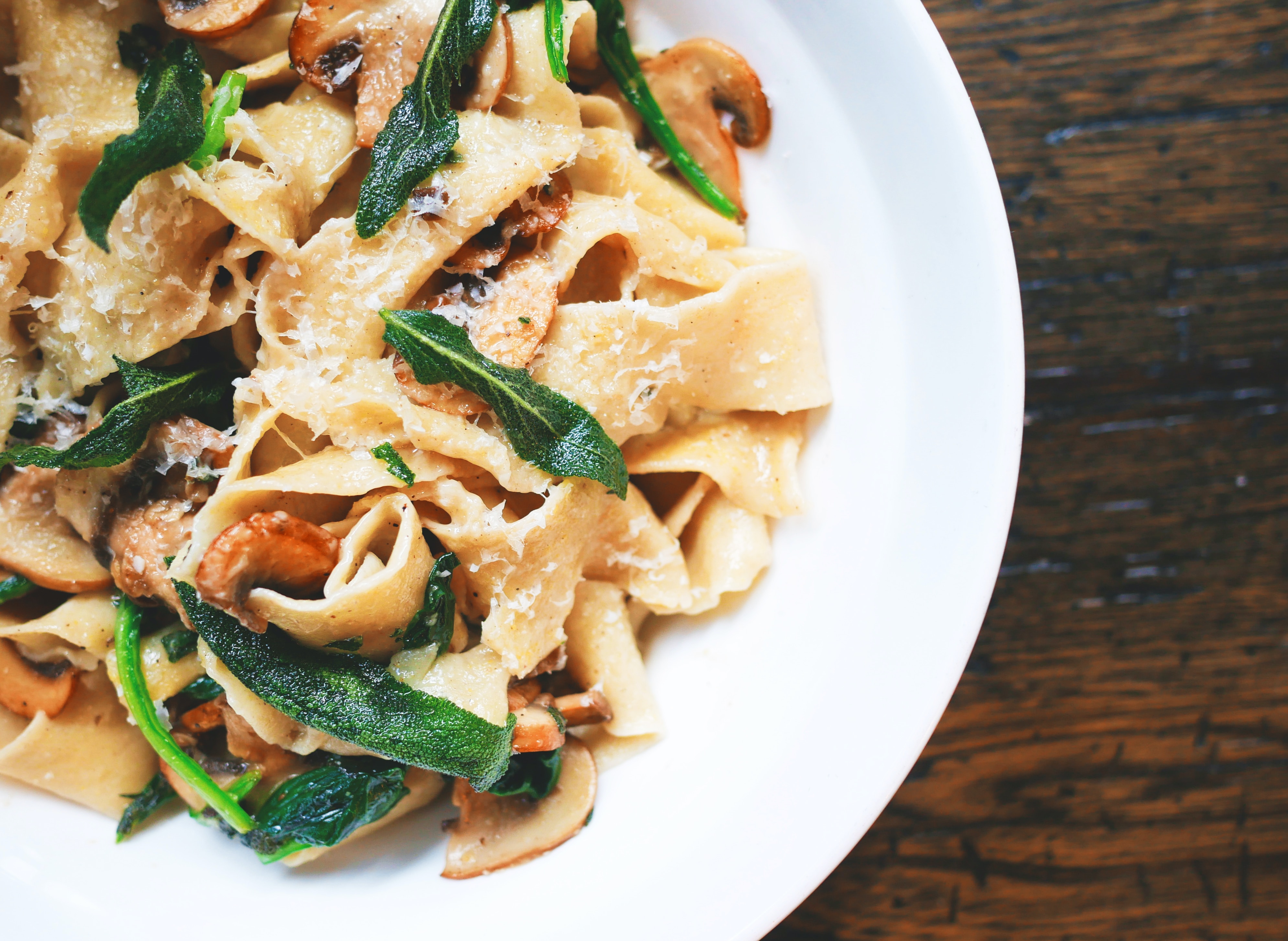 Plate of pappardelle pasta with mushrooms and green leafy vegetable