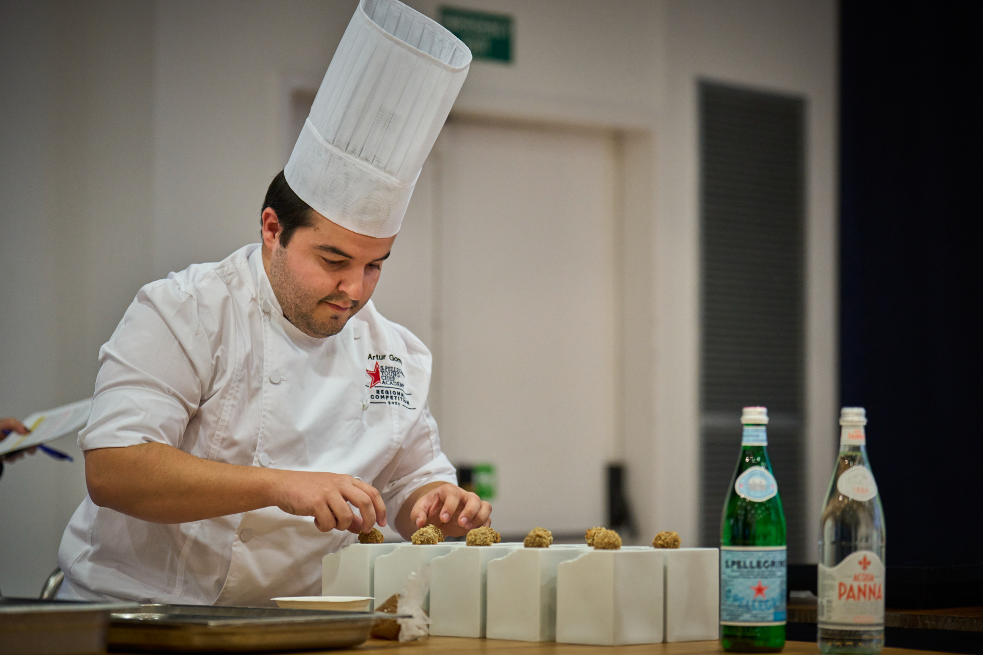 Chef in tall hat and white jacket prepping food with bottles of San Pellegrino and Acqua Panna