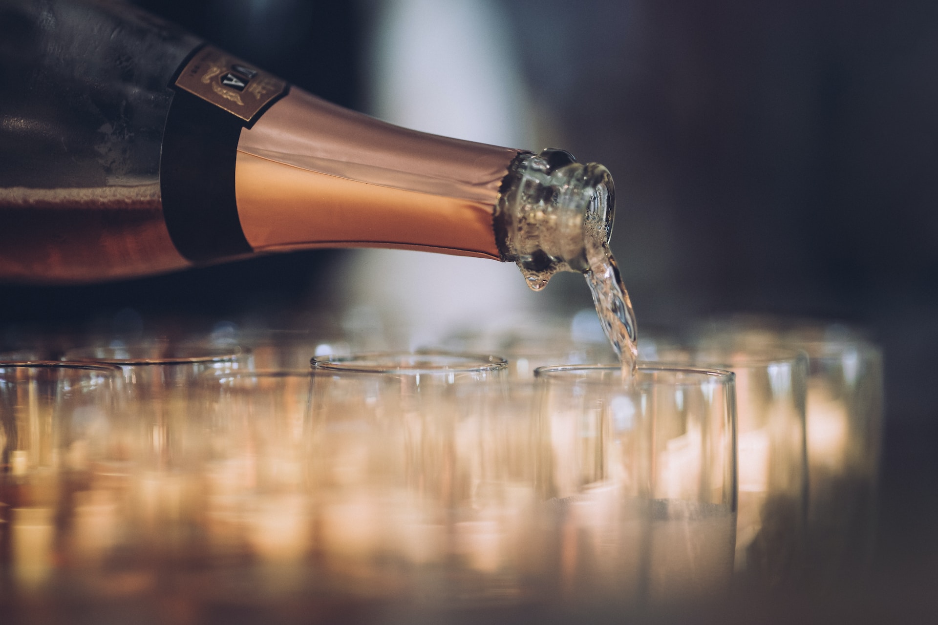 Close-up of a bottle of sparkling wine being poured into lots of flutes