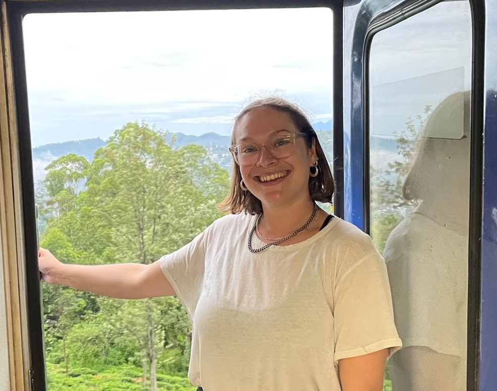 Rosie Raynor Law standing inside the open door of a train with countryside backdrop