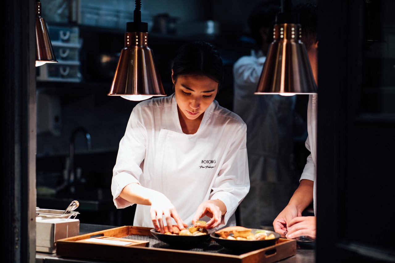 Chef Pam Soontornyanakij plating up food under lamps with dark kitchen background