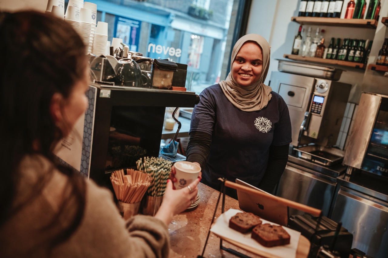 Halima, a barista at Arnabeet handing a coffee to a customer