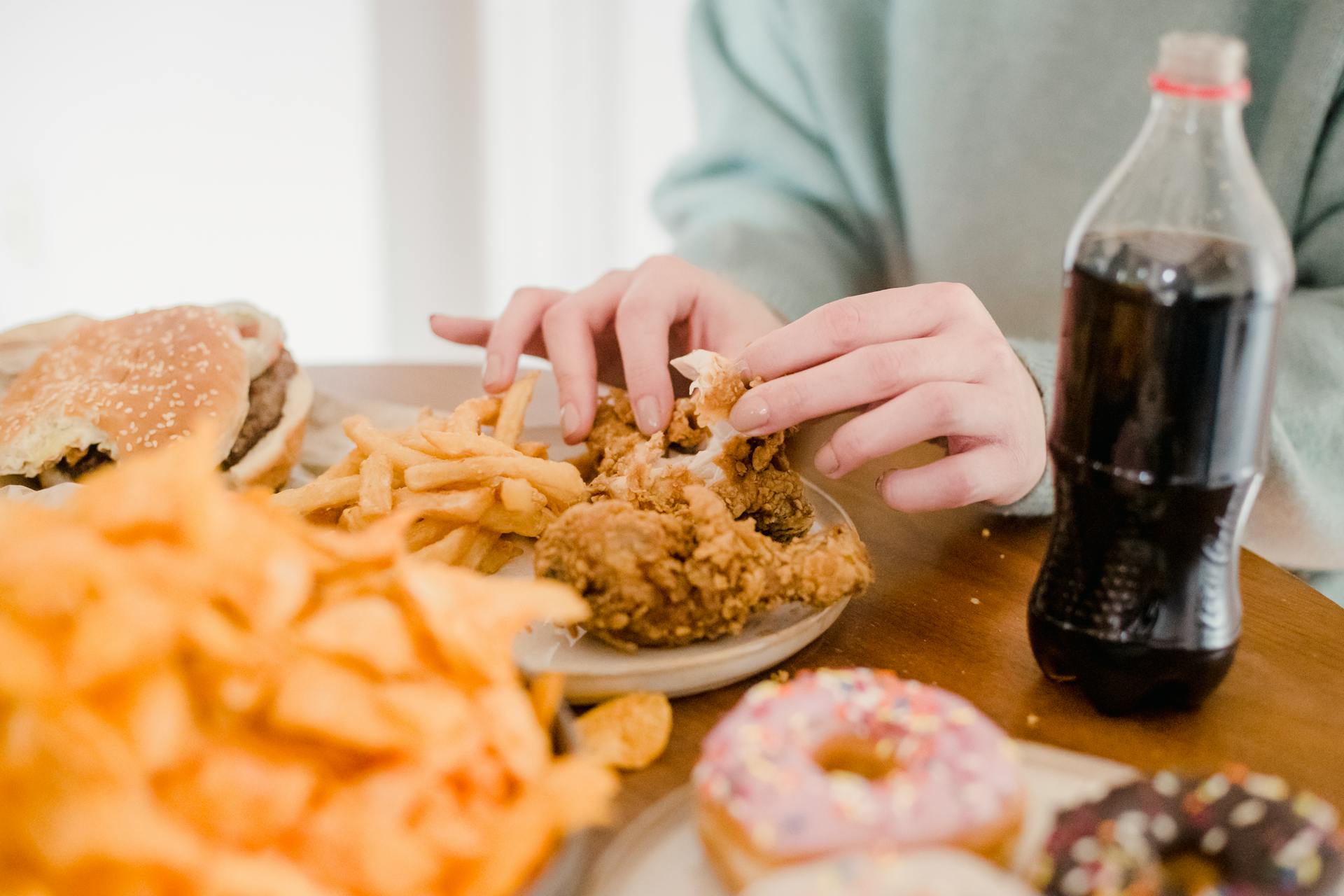 Person eating plate of fried chicken and chips, with other unhealthy food on table