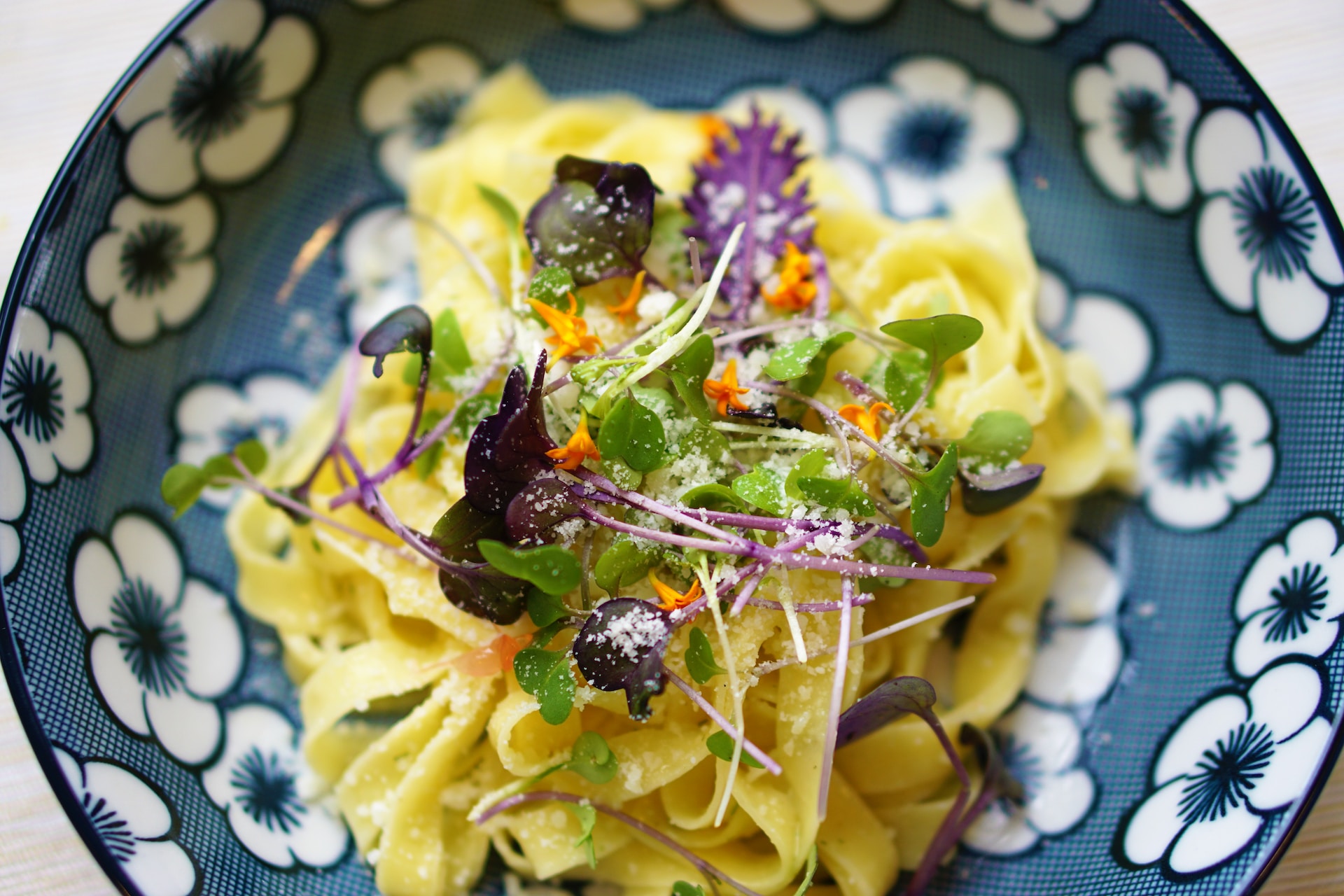 Close-up overhead shot of pasta dish in blue patterned bowl, topped with edible flowers
