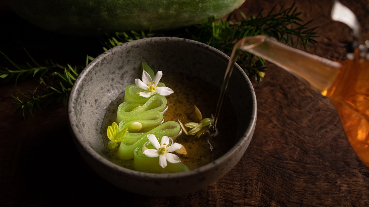 Amber liquid being poured into a bowl of beautiful food against a dark background