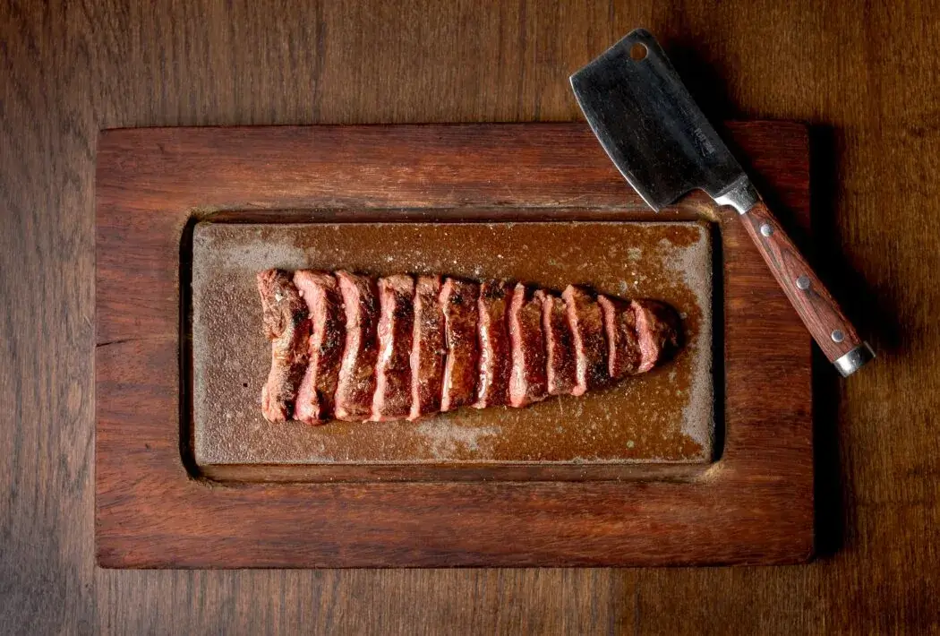 Overhead shot of a sliced steak on wooden board with a cleaver to the top right of the shot