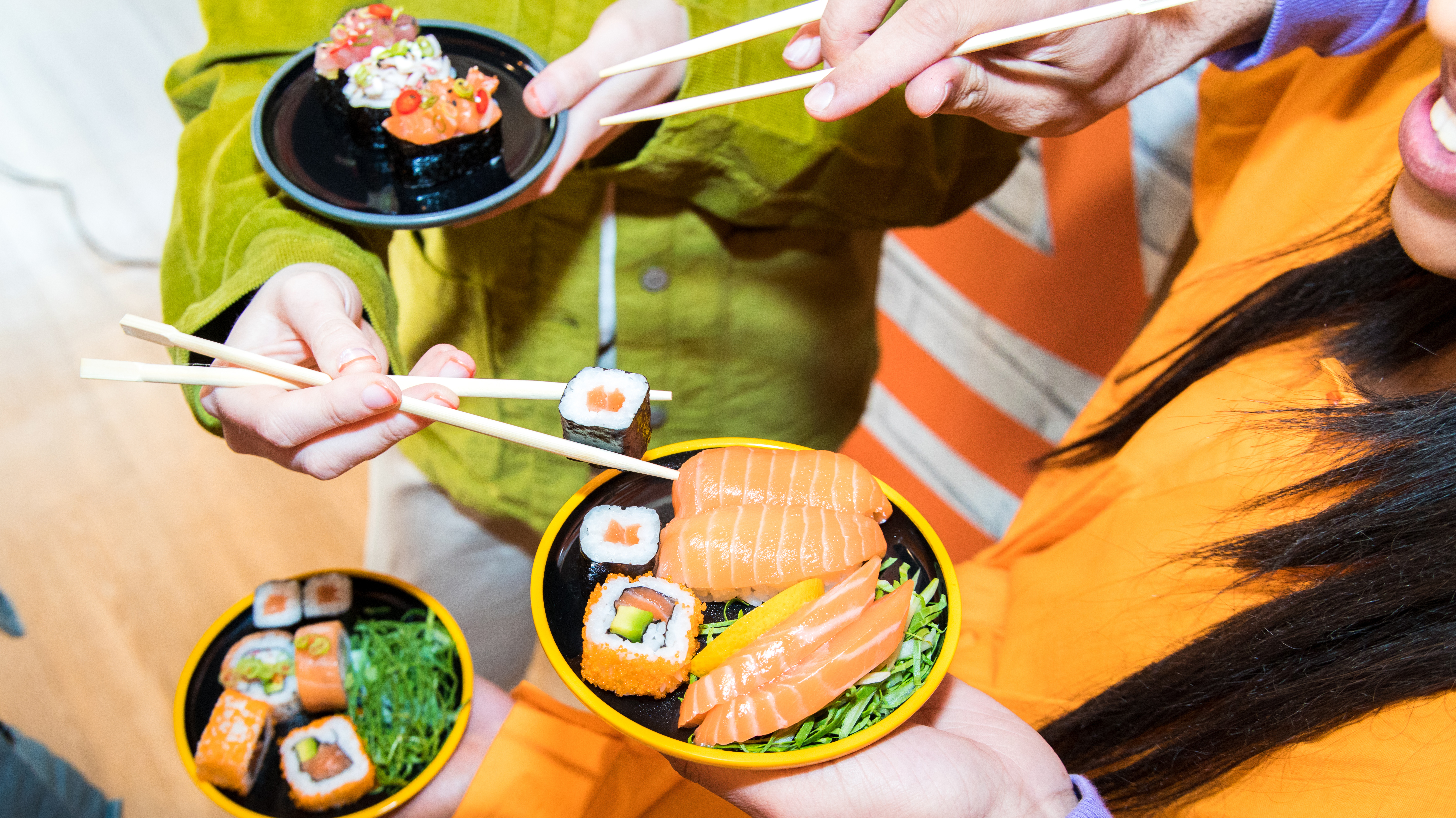 People holding colourful sushi dishes at Yo! Sushi