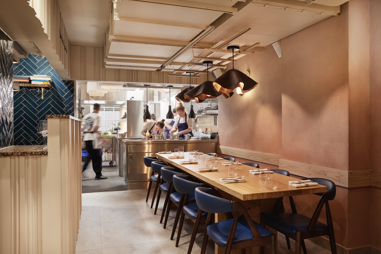 Apricity restaurant interior, with pink and gold decor and busy open kitchen in the background