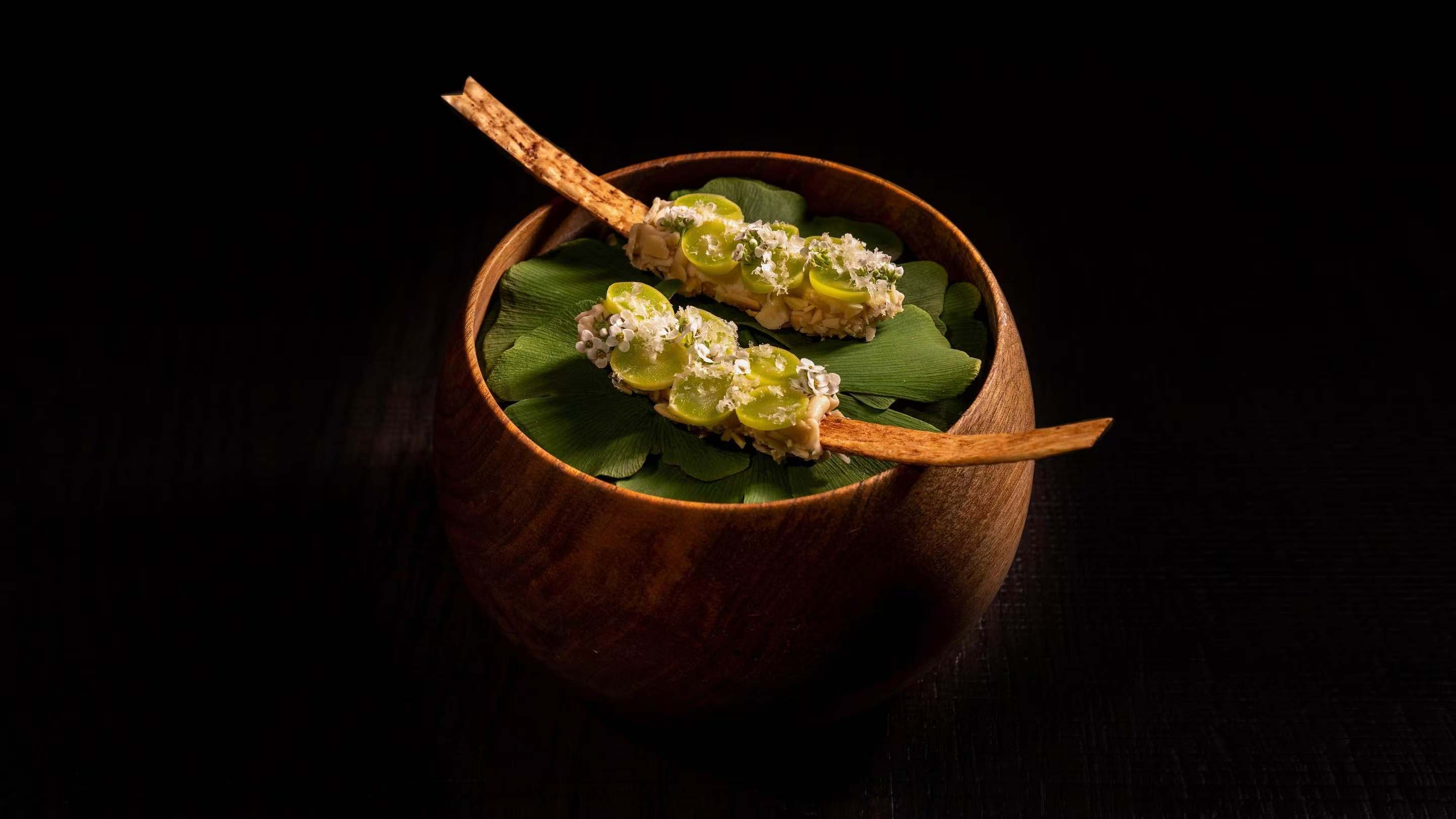 Two wooden spoonfuls of beautiful food in a wooden bowl against a dark background