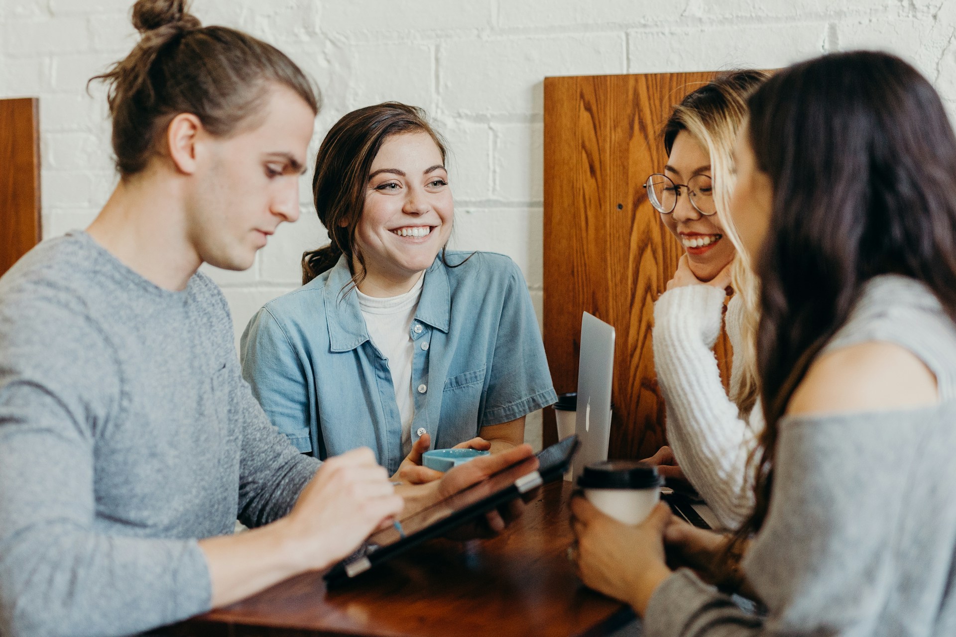 Four friends smiling while using a tablet and a laptop to learn
