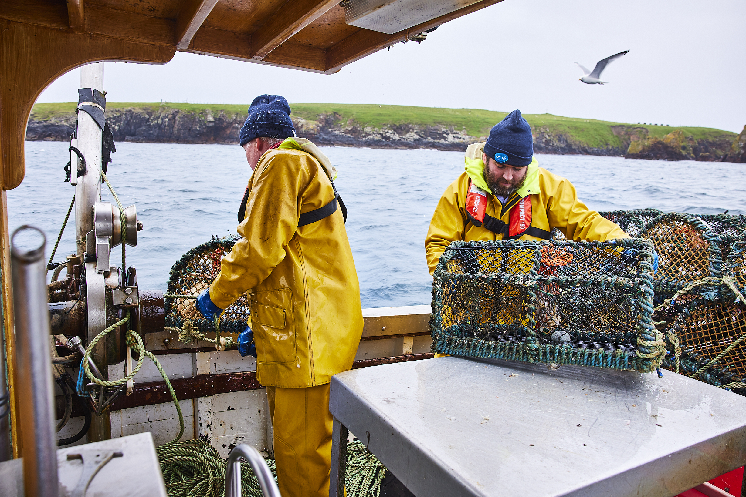 Two men crab fishing on boat wearing yellow waterproof overalls