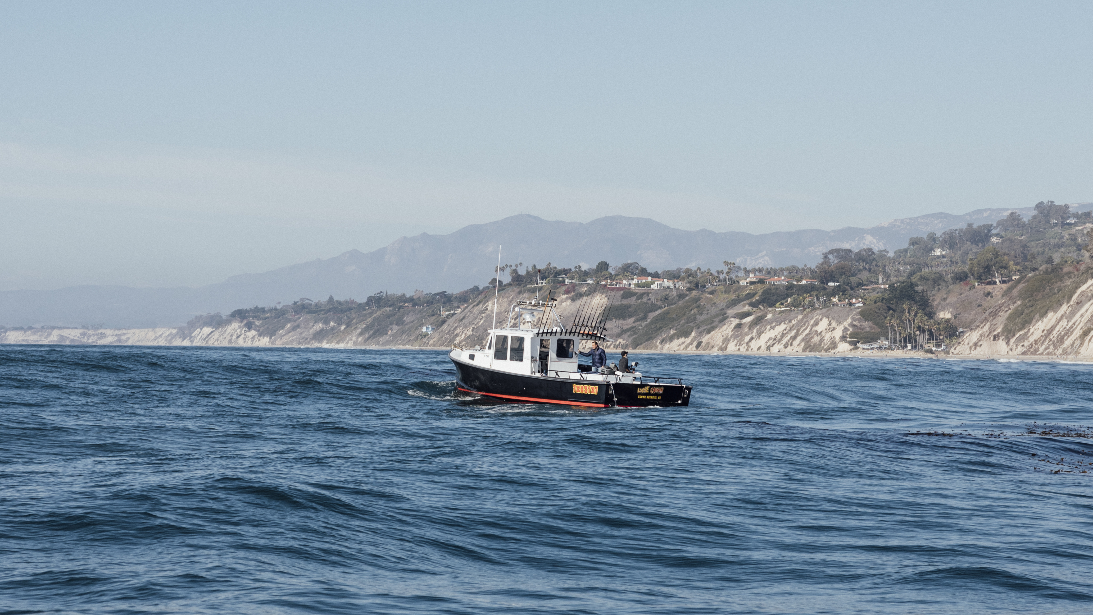 A small boat in the sea on a sunny day with cliffs in background