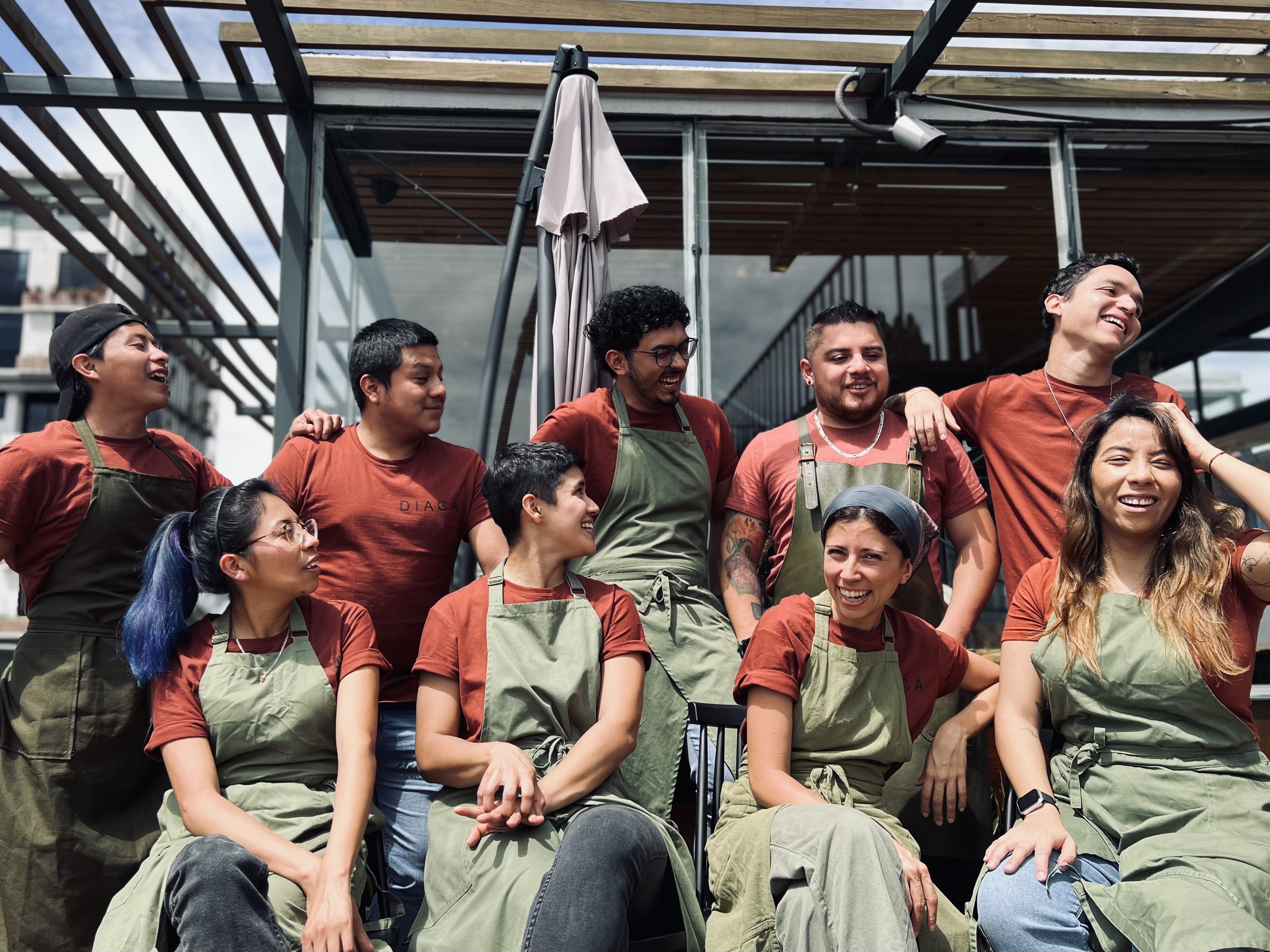 A group of cooks sitting in the sunshine wearing red t-shirts and green aprons