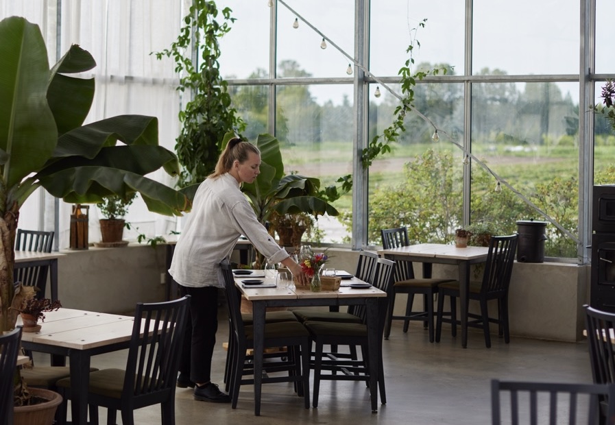 A server setting the table in a restaurant, with a large window in the background showing fields