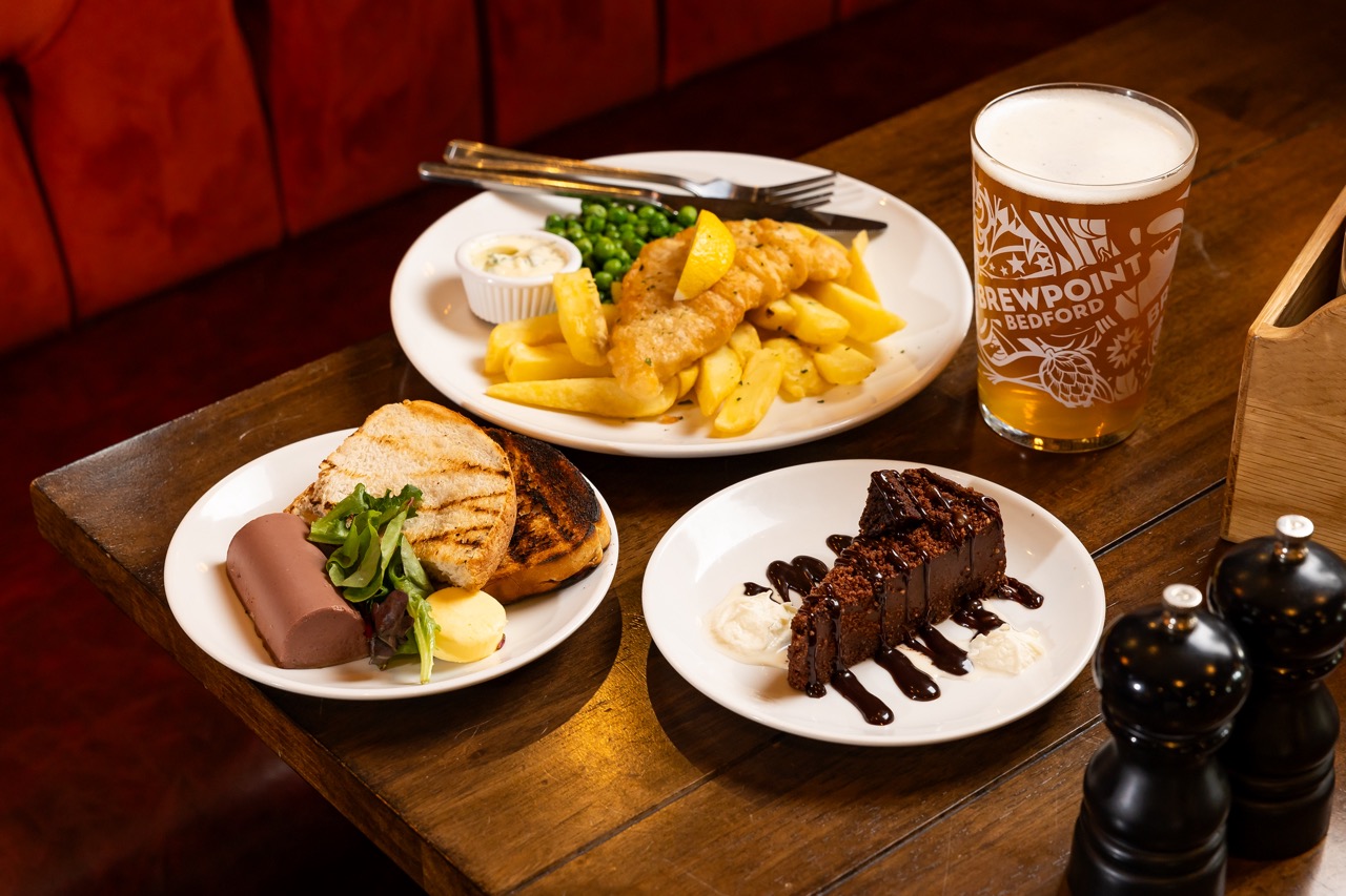 British pub food on wooden table: paté, fish and chips and chocolate cake, with pint of beer