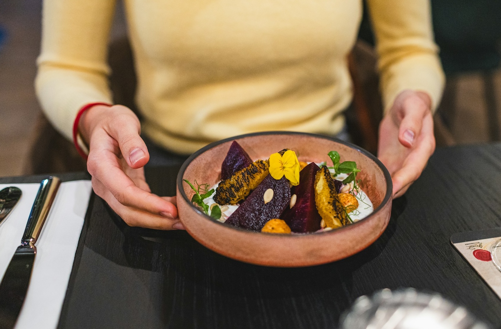 A woman in a yellow jumper holding a bowl of healthy food on a restaurant table