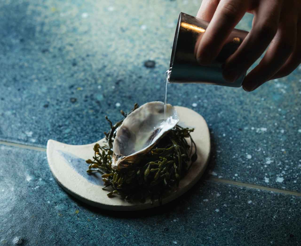 A drink being poured into an oyster shell at De Vie bar, Paris