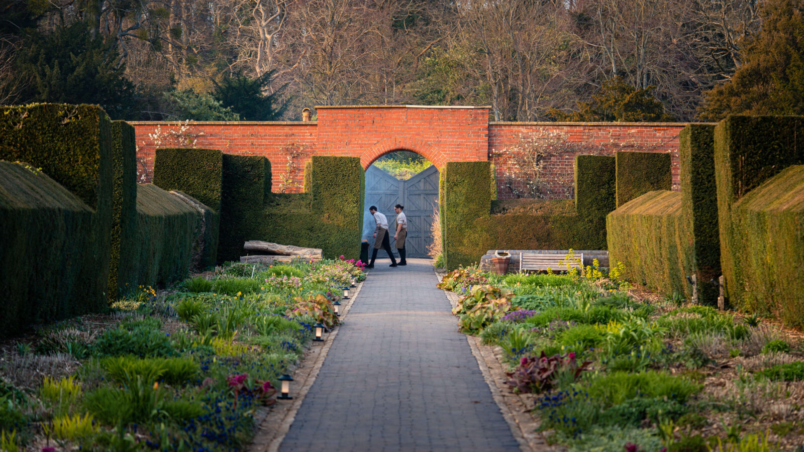 People walking through an archway out of a walled garden with forest in the background