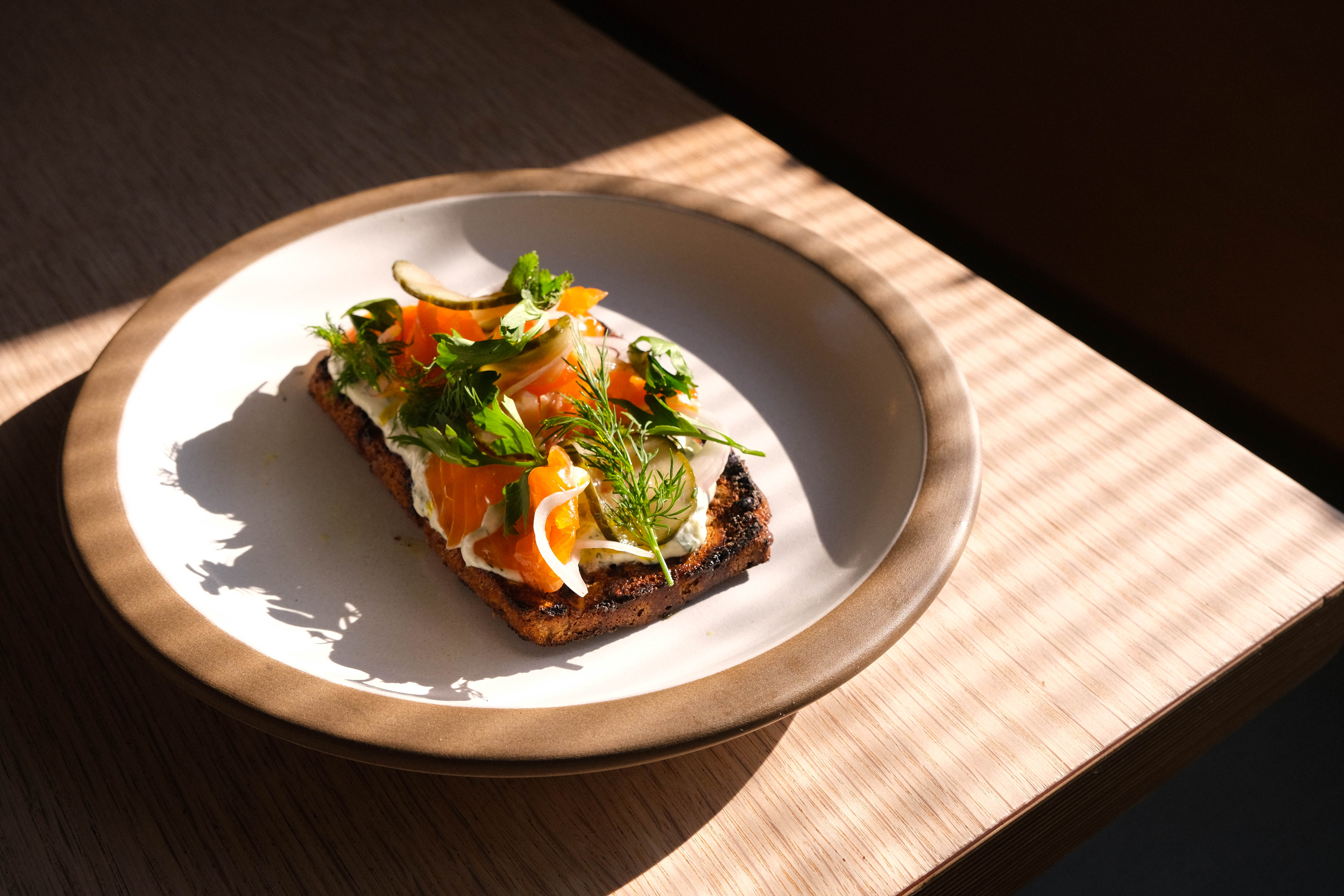 Chalk Stream Trout dish at Ozone Coffee, on wooden table in strong sunlight with shadows