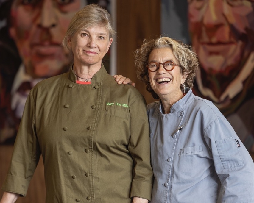 WCK Chef Corps Chefs Mary Sue Milliken and Susan Feniger smiling with murals in background